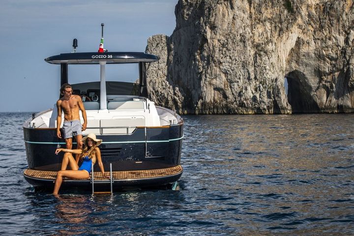 El Apreamare Gozzo 35 junto a los acantilados, con dos huéspedes en la plataforma de baño
