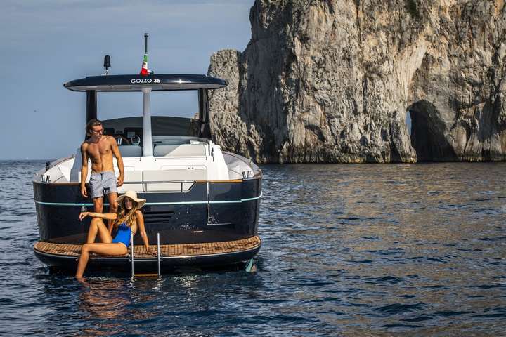 Guests on the swim platform of the Apreamare Gozzo 35, the Faraglioni of Capri behind