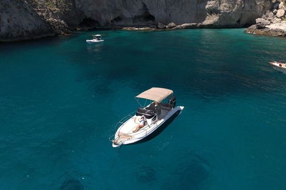 Un barco privado en agua turquesa bajo los acantilados